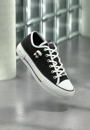 Zwarte canvas sneakers hebben witte accenten, een ronde neus, een gestructureerde zool en een kenmerkend logodetail. De veters zijn wit en hebben oogjes.