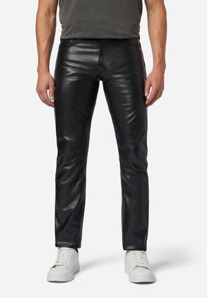 Schwarze Lederhosen mit glatter Textur, schlankem Schnitt und sichtbaren Nähdetails. Kombiniert mit weißen Sneakers.