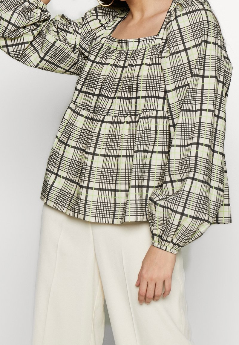 Blouse à carreaux vert clair et noir avec un décolleté carré, manches longues bouffantes et détails froncés à la taille.
