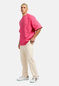 Lyserød oversized t-shirt med korte ærmer og broderet logo, der er sat sammen med cremefarvede sweatpants og multikolorede sneakers.