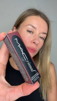Rouge à lèvres mat dans une boîte bordeaux avec des accents noirs, avec un texte blanc. Le modèle le tient près de son visage, montrant les détails du produit.