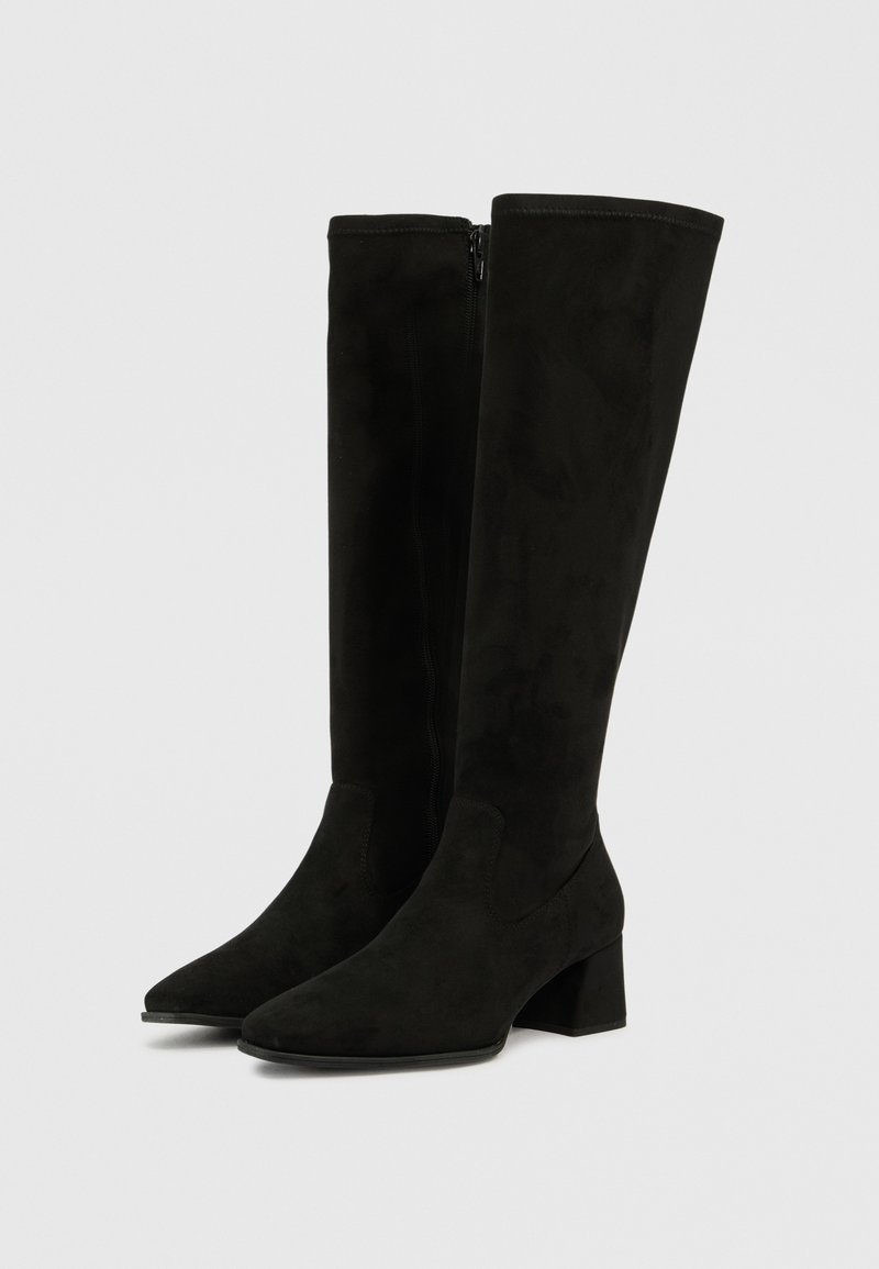 Botas altas de ante negro hasta la rodilla con puntera afilada, tacón cuadrado grueso y cierre lateral con cremallera. Textura suave con acentos mínimos.