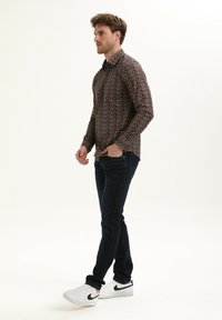 Heren overhemd met lange mouwen in een donker bloemmotief, gecombineerd met donkere jeans en witte sneakers. Het overhemd heeft een knoopsluiting bij de kraag en een slim fit.