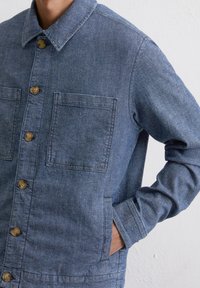 Spijkerjasje met kraag, knoopsluiting, twee voorzakken en lange mouwen. Gestructureerde, middelblauwe stof met een losse pasvorm.