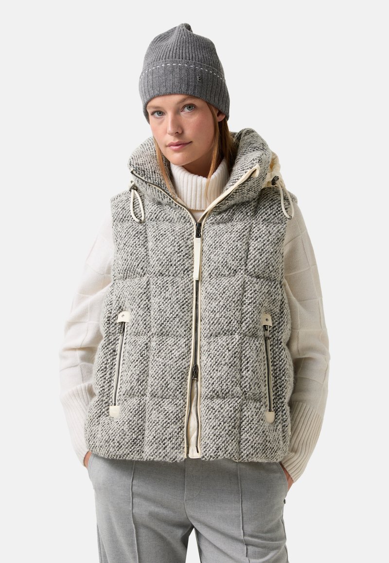 Szary pikowany kamizelka z tkaniny o teksturowanym wzorze, z zapięciem na zamek, dwiema bocznymi kieszeniami i kapturem. Nosi się ją na białym swetrze.