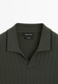 Polo shirt in dark green, made of 100% cotton. Features a ribbed texture, a collar with black accents, and vertical stripes.