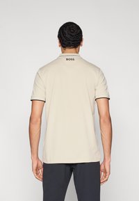 Bézs színű galléros póló fekete szegéllyel a nyakon, hátul kicsi "BOSS" logóval. Simább anyag, rövid ujjú, laza fazon.