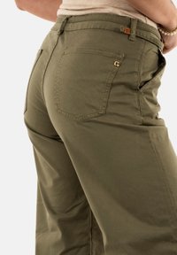 Pantaloni a gamba larga verde oliva realizzati in tessuto morbido. Presentano due tasche posteriori e un piccolo etichetta logo in vita, con dettagli di cucitura in vista.