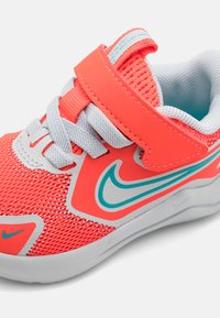 Baskets pour enfants Nike avec une tige en mesh corail vif, des accents blancs et une sangle velcro grise réglable. Dotées d'un détail de logo bleu.