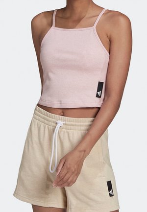 Vrouw draagt een lichtroze cropped tanktop en beige short met aantrekkoord, beide met Adidas-logo-tags op elk kledingstuk.