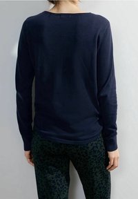 Maglione a maglia blu navy con maniche lunghe e scollo ampio, abbinato a pantaloni verde scuro con un delicato motivo a leopardo.
