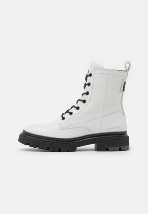 White leather ankle boot with black eyelets and laces, textured black rubber sole, and reinforced heel. Features a pull tab and brand insignia.