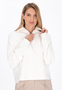 Hvid fleece-pullover med halvlukket krave, brede ærmer og ribbede manchetter. Blød tekstur og afslappet pasform. Bemærkelsesværdig sølvfarvet lynlåsdetalje.