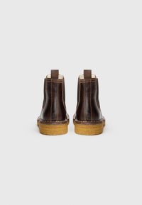 Barna bőr boka csizmák texturált oldalakkal, húzófülekkel hátul és kontrasztos bézs gumitalpakkal. Dupla varrás látható.