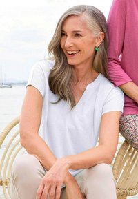 Witte katoen V-hals t-shirt met korte mouwen, gedragen door een persoon die op een rieten stoel zit, gecombineerd met lichtgekleurde broek.