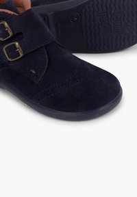 Pantofi din suede albastru-marinar cu două curele cu cataramă, detalii perforate și o talpă din cauciuc texturat, proiectați pentru copii.