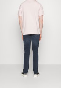 Camiseta de algodón rosa claro, vaqueros de mezclilla azul oscuro y deportivas negras con acentos texturizados. La vista muestra la parte posterior de la vestimenta.