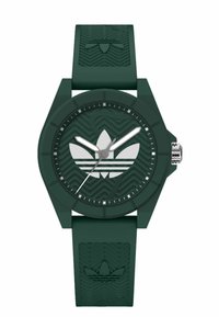 Montre en silicone verte avec un cadran rond, présentant des marquages horaires argentés, un logo à trois feuilles et un bracelet texturé avec un motif ondulé.