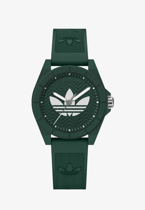 Zelené silikonové hodinky s kulatým ciferníkem, s kovovými hodinovými značkami, logem se třemi listy a texturovaným páskem s vlnitým vzorem.