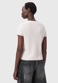 Maglione corto a maniche corte in un delicato rosa, realizzato in materiale morbido e peloso. Il design include un collo rotondo e un orlo a costine. Abbinato a jeans in denim scuro.