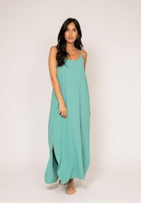 Une robe maxi sans manches de couleur turquoise, à coupe décontractée, avec des fentes latérales et une texture douce, accompagnée de sandales à lanières.
