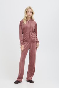 Tuta in velluto rosa polveroso, con felpa con zip e tasche frontali e pantaloni a gamba larga. Texture morbida e vestibilità rilassata.