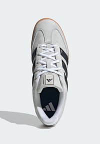 Sivé semišové tenisky s čiernymi pruhmi, bielymi šnúrkami a bielou gumovou podrážkou. Majú logo na jazyku a textúrovaný interiér.