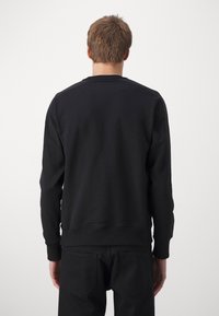 Svart sweatshirt med långa ärmar, ribbade muddar och midja. Slät textur, enkel design och inga synliga logotyper. Bakvy visas.