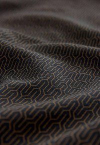 Textil con un fondo oscuro que presenta un patrón geométrico en dorado. La tela muestra una textura suave y un ligero caído.