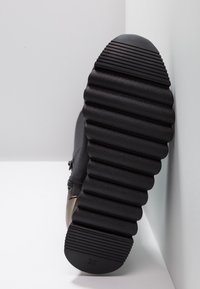 Semelle de sneaker noire avec un motif ondulé en relief, dotée d'une coque de protection lisse et noire à l'avant et du numéro "36" embossé sur la semelle.