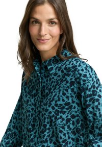 Knopfhemd in Türkis mit schwarzem Leopardenmuster, mit Kragen und weichem Stoff. Details umfassen eine Knopfleiste und eine lockere Passform.