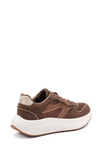 Zapatilla de ante marrón y malla con entresuela blanca, forma redondeada y costuras de acento sutil. Cuenta con un diseño de cordones y detalles texturizados.