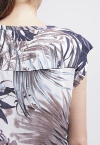 Blusa leggera con stampa botanica nei toni di marrone, blu e bianco. Maniche a cappuccio e un collo strutturato discreto.