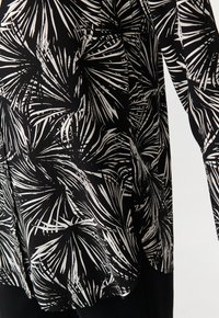 Camicia in tessuto nero con un audace motivo di foglie di palma bianche, maniche lunghe e una vestibilità rilassata. Texture liscia con un design fluido.