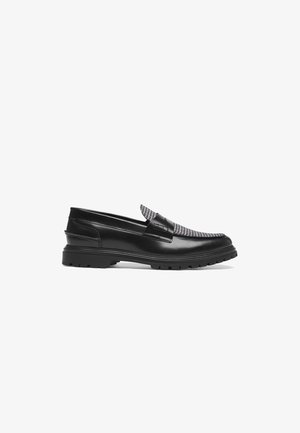 Mustad nahast loafers halli ja musta ruudulise pealmise osaga, millel on madal ja jäme tald ning dekoratiivne rihm.