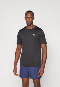 Black sports t-shirt in lightweight, breathable fabric, featuring a round neckline and short sleeves. Small white logo on the chest.