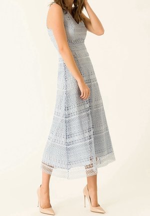 Robe en dentelle bleu clair avec un corsage ajusté, une silhouette en A et des motifs décoratifs. Associée à des talons hauts nude.