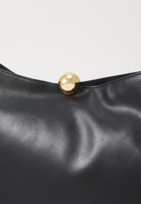 Borsa a mano in pelle nera caratterizzata da una texture liscia e una chiusura rotonda in oro con il nome del marchio impressa.
