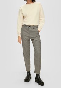 Sweatshirt crème avec des poignets côtelés, associé à un pantalon à motif pied de poule noir et blanc. Le modèle porte des bottines épaisses noires.