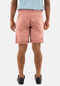 Shorts in cotone rosa chiaro con risvolti, dotati di due tasche posteriori e una zip, indossati con scarpe nere.