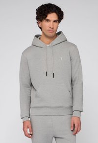 Světle šedá mikina s kapucí vyrobená z měkké látky, obsahující klokaní kapsu, nastavitelné šňůrky a malé logo na hrudi.