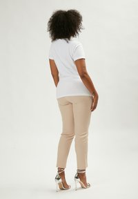 Camiseta blanca, de mangas cortas, diseño ajustado, combinada con pantalones beige ajustados. Calzado: sandalias plateadas de tacón alto con tiras en el tobillo.