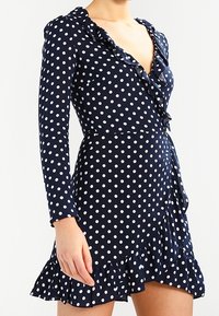 Námořnické šaty s puntíky, dlouhými rukávy, volánkovým výstřihem a lemem, s designem do zavinování, které mají bílé puntíky a mírně rozšířenou sukni.