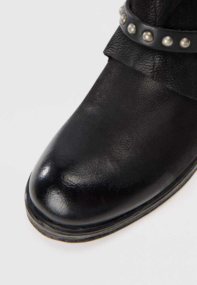Schwarze Leder-Stiefelette mit runder Zehenpartie, strukturiertem Material und einem Riemen mit silbernen Nieten um den Knöchel. Flache Sohle mit Nähdetails.