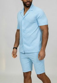 Chemise bleu clair à manches courtes avec fermeture à bouton et short assorti. Tissu texturé, coupe décontractée, design minimal.