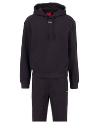 Svart huvtröja med snoddar och logotyp på bröstet, tillsammans med matchande svarta sweatpants. Båda är tillverkade av mjukt tyg med en avslappnad passform.