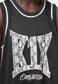 Maillot de basket en mesh noir avec un grand texte "K1X" à motif serpent blanc et "OUTTA THIS WORLD" en typographie stylisée.