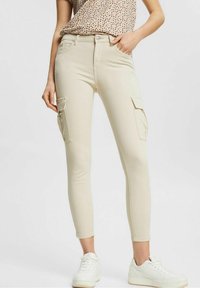 Beige cargobroek met twee zijzakken, aansluitend ontwerp, lichte stretch en een soepele textuur, gecombineerd met witte sneakers.