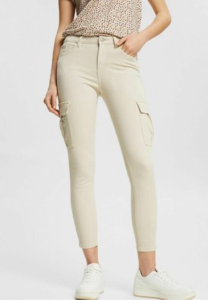Pantalones estilo cargo en color beige con dos bolsillos laterales, diseño ajustado, ligera elasticidad y una textura suave, combinados con zapatillas blancas.