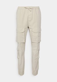 Béžové cargo kalhoty s elastickým pasem a šňůrkou. Mají několik bočních kapes a zúžené kotníky. Bavlněná tkanina s hladkou texturou.